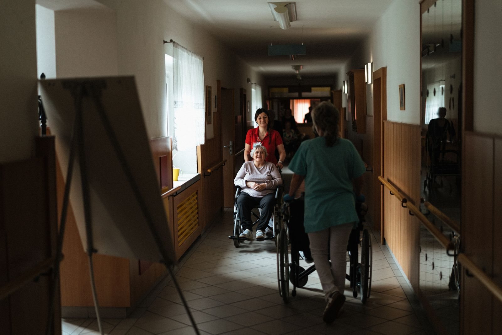 Staff walking residents in wheelchairs along a corridor