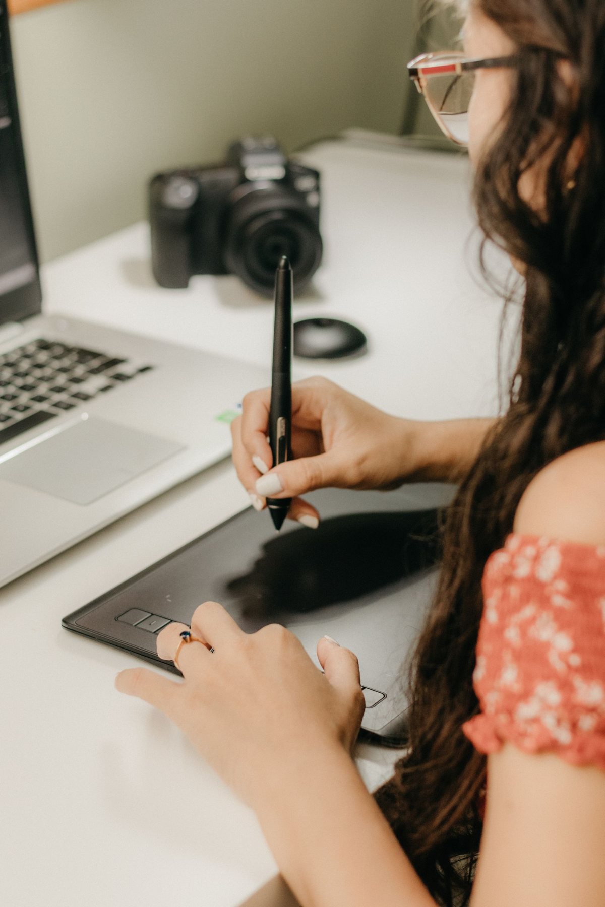 A designer drawing on a graphics tablet beside a camera and laptop