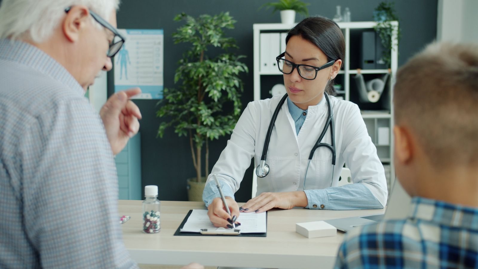 A doctor taking notes while speaking with an older patient and a boy