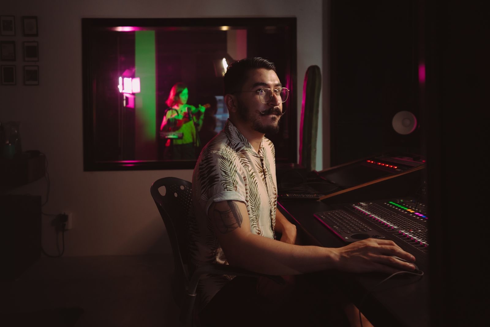 An engineer at a mixing console with the live room behind the glass