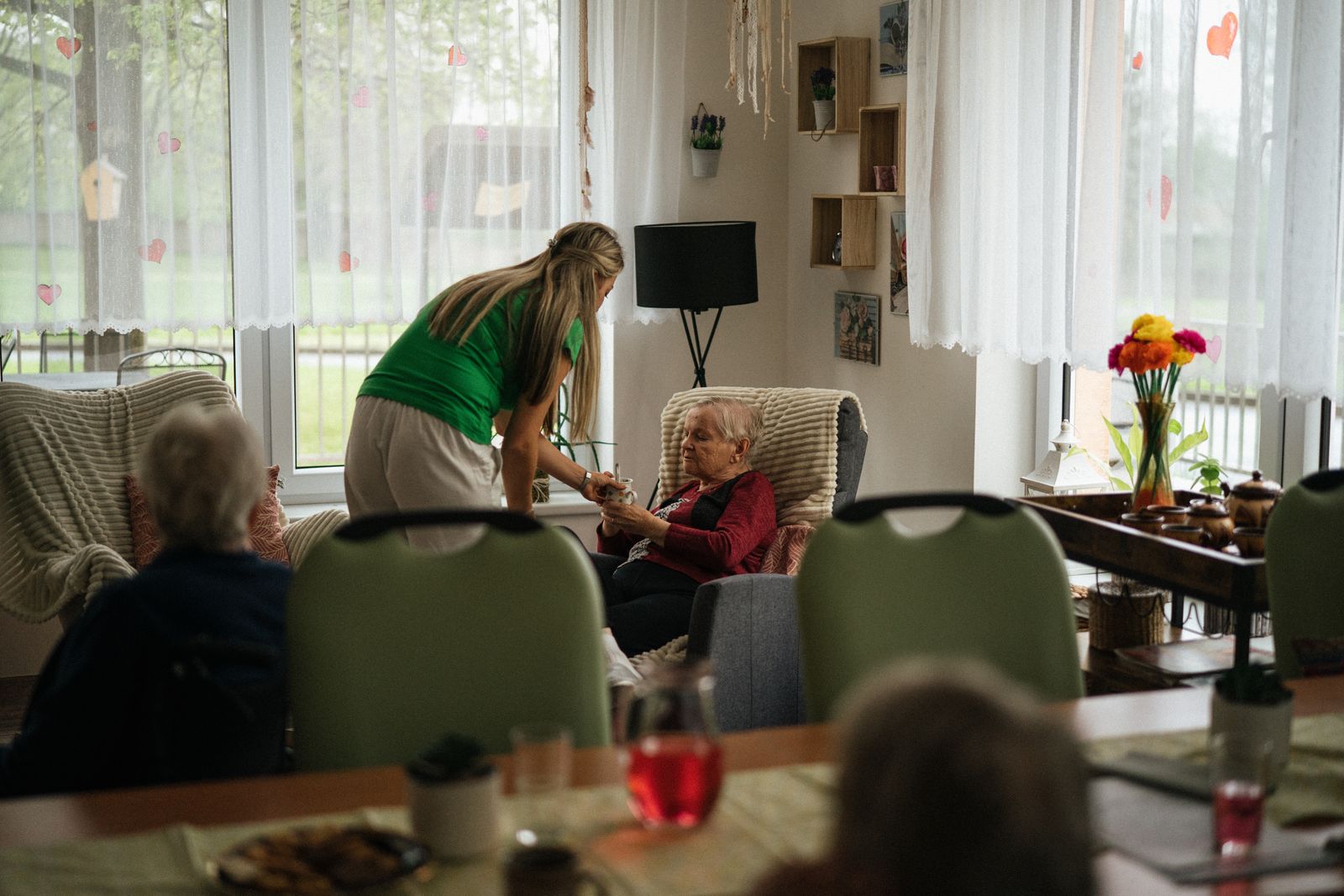 A caregiver serving tea to residents in a sunny lounge